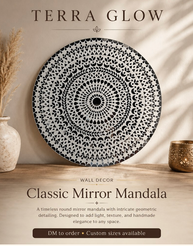 A round black-and-white mirror mandala wall decor piece displayed on a wooden surface against a beige wall, with decorative dried grass in a vase on the left and a small metallic bowl on the right. Text at the top reads 'TERRA GLOW' and the product name 'Classic Mirror Mandala' appears below.